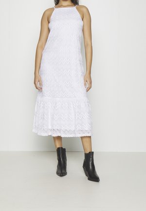 Biała sukienka halter z koronką, z wzorem zygzaków i falbanowym dołem, w zestawieniu z czarnymi botkami za kostkę. Gładka faktura i luźny krój.