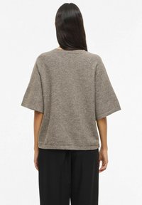 Pelēks adīts tops ar īsām, plati izklātām piedurknēm, apaļu kakla izgriezumu un vaļēju pieguļojumu, kopā ar melnām biksēm. Gluda tekstūra un smalkas šuves.