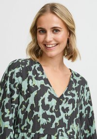 Rochie neagră și verde menta cu decolteu în V, având un model abstract texturat și mâneci largi. Țesătura pare ușoară și fluidă.