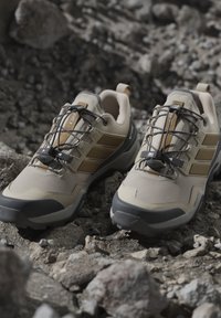 Scarpe da escursionismo beige e marroni con sistema di lacci rapidi neri poggiate su un terreno roccioso.