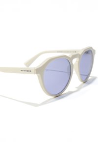 Osmiboké sluneční brýle s krémovým plastovým rámem a fialovými tónovanými čočkami. Na nožičce je logo značky a mají hladkou, lesklou texturu.