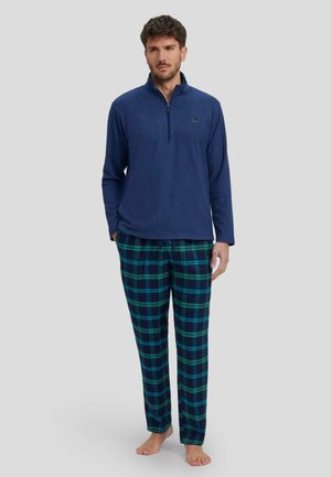 Sudadera de forro polar azul marino con cuello de media cremallera, combinada con pantalones de lounge de cuadros verdes y azules, que cuentan con un corte relajado y una textura suave.