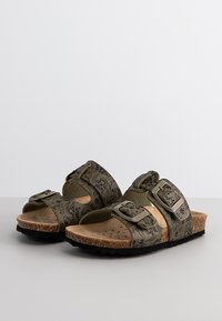 Sandalias verdes de dos correas con hebillas ajustables. Plantilla de corcho y suela de goma texturizada, con un patrón en las correas superiores.