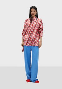 Colorful patterned shirt in shades of pink and red; paired with loose blue trousers. Footwear features bold red accents.
