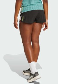 Svarta träningsshorts med vita och neongröna accenter, tillsammans med grå sneakers och vita ankelsockor. Shortsen har en slank, åtsittande design.