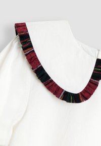 Haine albă cu guler larg, rotunjit, finisat cu stofă în carouri roșu, verde și negru, cu margine cu volane.