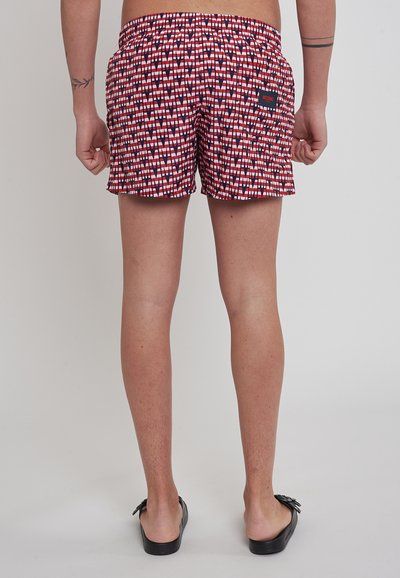 Pantaloni da bagno rossi con un design a pattern in bianco e nero. Vita elasticizzata, tasche laterali e una piccola etichetta del marchio sul retro.