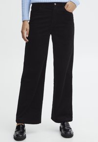 Zwarte corduroy wijde broek met verticale ribbeling, hoge taille, zijzakken en een knoopsluiting. Gepaard met zwarte loafers.