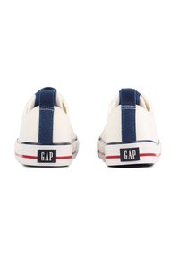 Creme kleurige canvas sneakers met veters, navy accent aan de achterkant, witte zool, rode streep en GAP-logo op de hiel. Gladde textuur. Laag profiel ontwerp.