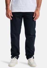 Navyblauwe katoenen broek met een rechte pasvorm, voorzien van riemlussen en zijzakken, gecombineerd met witte sneakers. Gladde textuur.