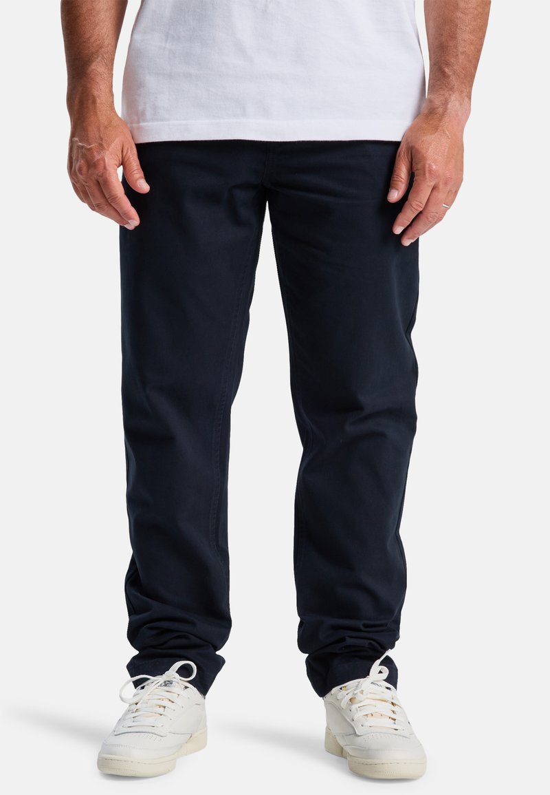 Navyblauwe katoenen broek met een rechte pasvorm, voorzien van riemlussen en zijzakken, gecombineerd met witte sneakers. Gladde textuur.