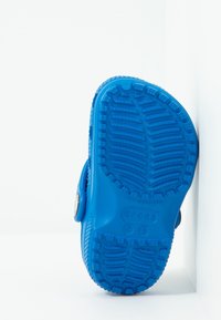 Modré dětské Crocs sandály s texturovanou podrážkou, stojící proti bílému pozadí.