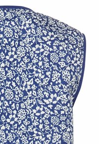 Quilted sleeveless top with a blue background featuring white floral patterns, finished with contrasting trim along the edges.