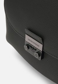 Sac en cuir texturé vert foncé de forme arrondie, doté d'un élégant fermoir en métal avec la marque Emporio Armani et des accessoires décoratifs en métal.