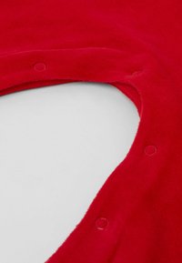 Tissu en polaire rouge avec une texture douce, comportant une découpe en forme de cœur et des fermetures à pression le long du bord pour une fermeture sécurisée.