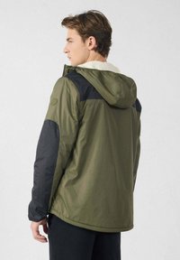 Groen-zwarte capuchonjas met een platte kraag, waterafstotend materiaal en een gladde textuur. Heeft een logo op de schouder en een zachte voering.