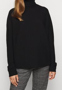 Svart polotröja med långa ärmar, en avslappnad passform och ribbade muddar, i kombination med grå rutiga byxor. Mjuk, medelviktig tyg.