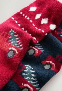 Dos mantas de peluche: una roja con patrones de diamante blancos y árboles, la otra azul marino con camiones rojos y árboles, ambas texturizadas y acogedoras.