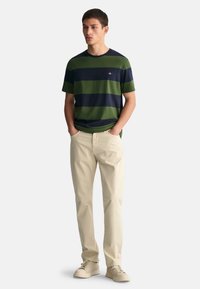 Herre kortermet t-skjorte i mørk marineblå med grønne horisontale striper. Kombinert med beige bomullsbukser og lyse sneakers.