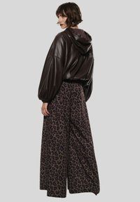 Felpa con cappuccio in finta pelle marrone dal taglio morbido e cappuccio con lacci, abbinata a pantaloni a gamba larga con un motivo a macchie di leopardo scure.