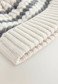 Bonnet en tricot avec une texture côtelée crème et un motif gris. Le design inclut un revers replié pour plus de chaleur. Matériau en laine douce.