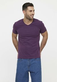 Paarse V-hals T-shirt van zachte katoen, korte mouwen, met een subtiele logo op de borst, gecombineerd met blauwe denim shorts.