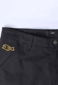 Pantalon noir en tissu solide, avec un logo de poisson brodé en jaune et une fermeture à bouton. Lignes épurées avec poches inclinées.