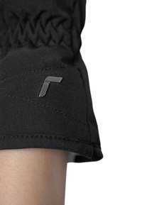 Schwarzer Stoff mit gesticktem Muster und einem metallischen Logoakzent. Der gesäumte Ärmel gefällt durch seine glatte Textur und taillierte Passform.