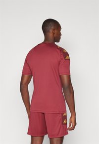 Bordeaux sportshirt met korte mouwen en bijpassende shorts. Kenmerkt zich door gouden logo-accenten op de schouders en shorts. Zachte stoftextuur.