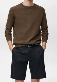 Pull marron texturé à manches longues et col rond, associé à un short noir, tous deux à coupe décontractée avec des poches latérales.