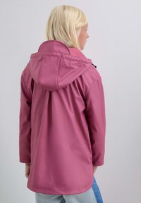 Chaqueta impermeable rosa con capucha, que presenta un corte holgado, mangas largas y una espalda ventilada. Textura suave, con acentos de hardware mínimos.