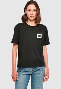 Tricou negru din bumbac cu guler rotund și mâneci scurte, având un logo pătrat alb cu un design negru în zona stângă a pieptului.