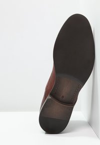 Scarpa in pelle marrone con tomaia texturizzata, punta liscia e suola piatta in gomma. Riporta la taglia 42 sulla suola.
