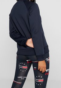 Sudadera azul marino con puños y dobladillo acanalados, con un corte relajado. Combinada con leggings ajustados que muestran patrones gráficos en rojo y blanco.