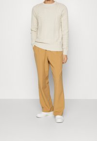 Maglione a costine color crema con maniche a coste, abbinato a pantaloni a gamba larga marrone chiaro. Sneakers bianche completano l'outfit.