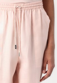 Light pink elastic-waist pants with a drawstring closure, featuring side pockets and a smooth, textured fabric.