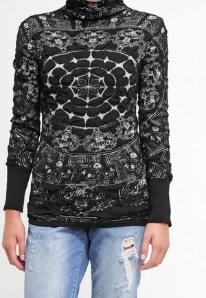 Haut à manches longues noir et blanc avec des motifs géométriques et floraux complexes, associé à un jean bleu clair déchiré.
