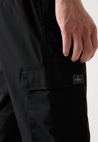 Zwarte cargobroek van een gestructureerde stof, met een zijzak en een Calvin Klein logo label. Het ontwerp heeft een moderne snit en een getailleerde pasvorm.