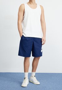 Biały top na ramiączkach z małym logo, granatowe spodenki, białe trampki z akcentami i białe skarpetki. Spodenki mają logo z boku i luźny krój.
