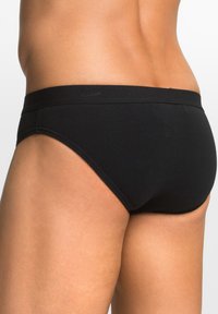 Slip da uomo nero realizzato in tessuto morbido. Presenta un cinturino liscio e cuciture minime, progettato per il massimo comfort e una vestibilità sicura.