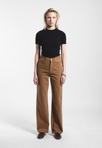 Camicetta nera a maniche corte abbinata a pantaloni larghi in cotone resistente a vita alta di colore marrone. Presenta tasche frontali classiche e chiusura con bottoni.