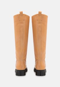 Botas altas de pele laranja com uma textura suave, apresentando uma sola de borracha preta e alças na parte superior para facilitar o calçar.