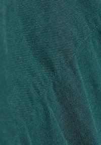 Tela color verde azulado con superficie suave y texturizada con un patrón diagonal. Material ligero y elástico, con un brillo sutil y tejido fino.