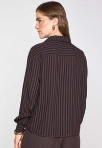 Camicia a maniche lunghe con righe verticali blu scuro e ruggine. Tessuto morbido e leggero. Presenta un colletto classico e maniche con polsini.