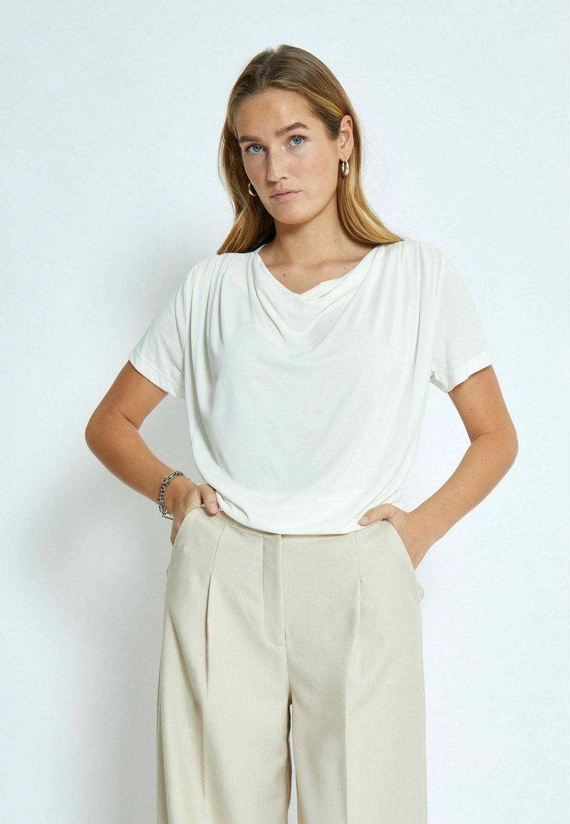 Vit draperad t-shirt i mjukt tyg med korta ärmar, kombinerad med beige högmidjade byxor med veck och sidofickor.