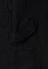 Yksityiskohta mustasta kankaasta, joka sisältää taskun erottuvalla ompelella. Materiaali näyttää kestävältä ja siinä on teksturoitu pinta.