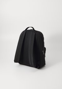 Černý batoh s zakřiveným designem, hladkým materiálem, síťovanou zadní stranou a bočními zipy. Má horní držadlo a decentní pruhované akcenty.