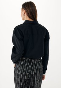 Černá košile s knoflíky a standardním límcem, doplněná o kalhoty s vysokým pasem a kostkovaným vzorem v černobílém provedení.