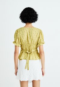 Gele blouse met korte puffmouwen, samengebonden taille en bloemenprint. Gecombineerd met een witte mini-jurk van textuur.