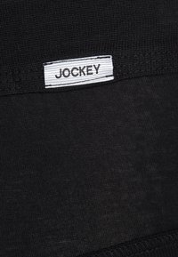 Sort stof med en glat tekstur har et hvidt JOCKEY mærke. Designet er simpelt og uden udsmykning, med fokus på funktionalitet.